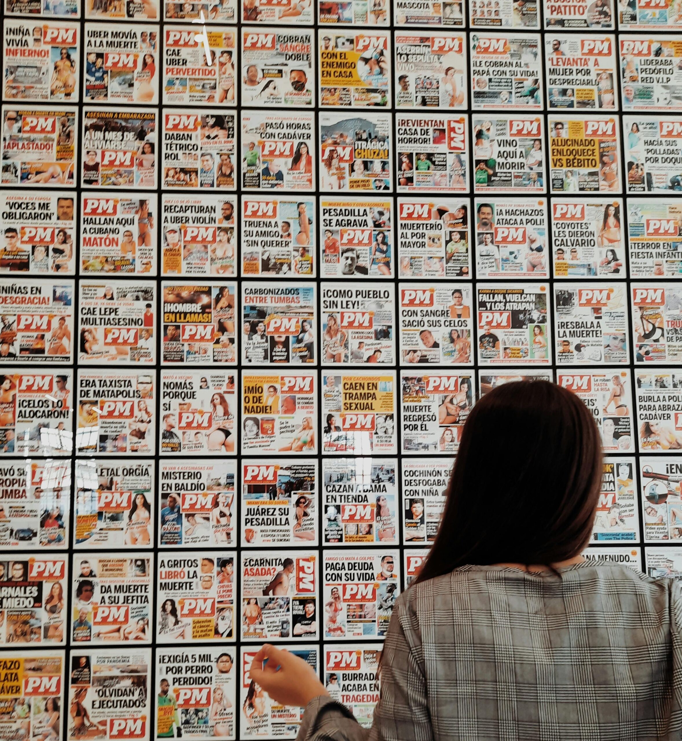 Woman examining a wall covered with PM magazine covers in Athens, Greece